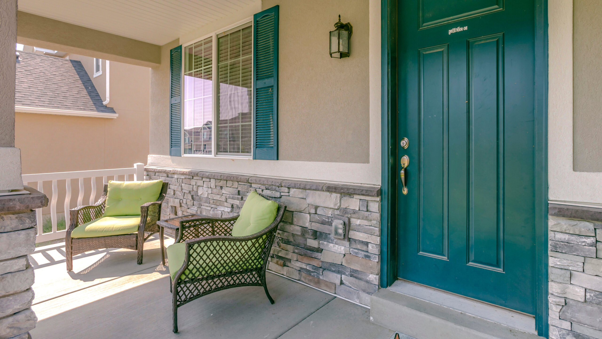 Top 5 Door Trends in 2025 for Modern Homes 4 A stylish front porch with a bold teal front door, wicker chairs with green cushions, stone accents, and a welcoming outdoor seating area.