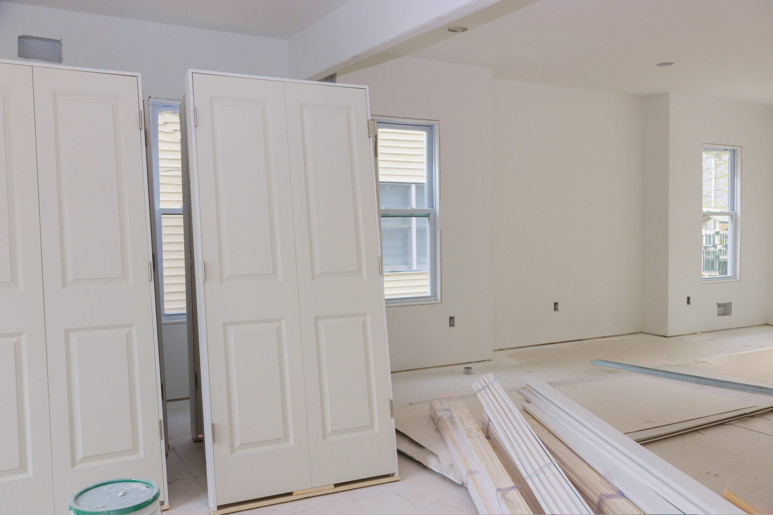 White pre-hung interior doors with hinges and partial frames leaning upright in a freshly painted room.
