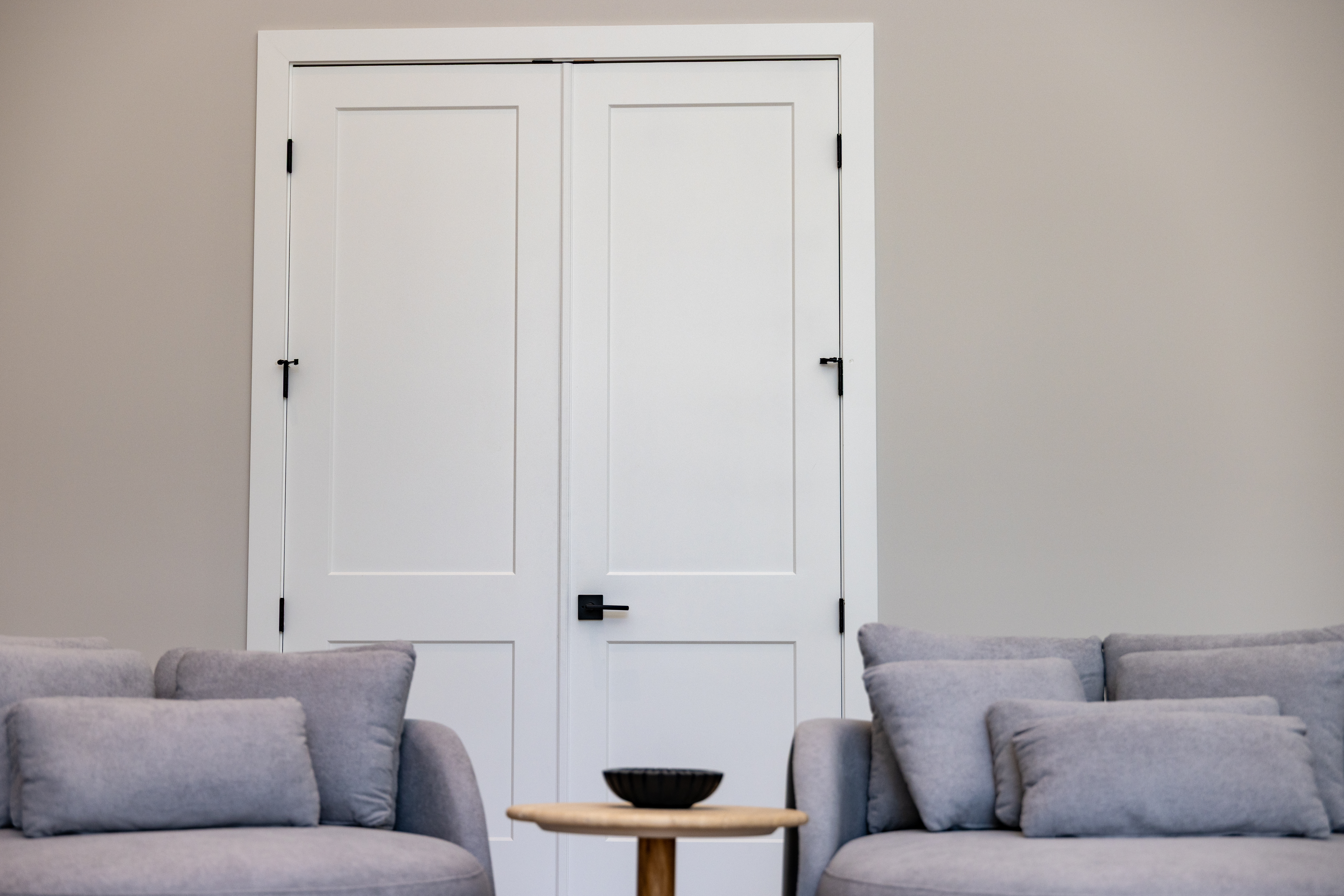 White double shaker-style doors installed by 1st Choice Door & Millwork, shown in a modern living room with gray sofas and a light wood side table.