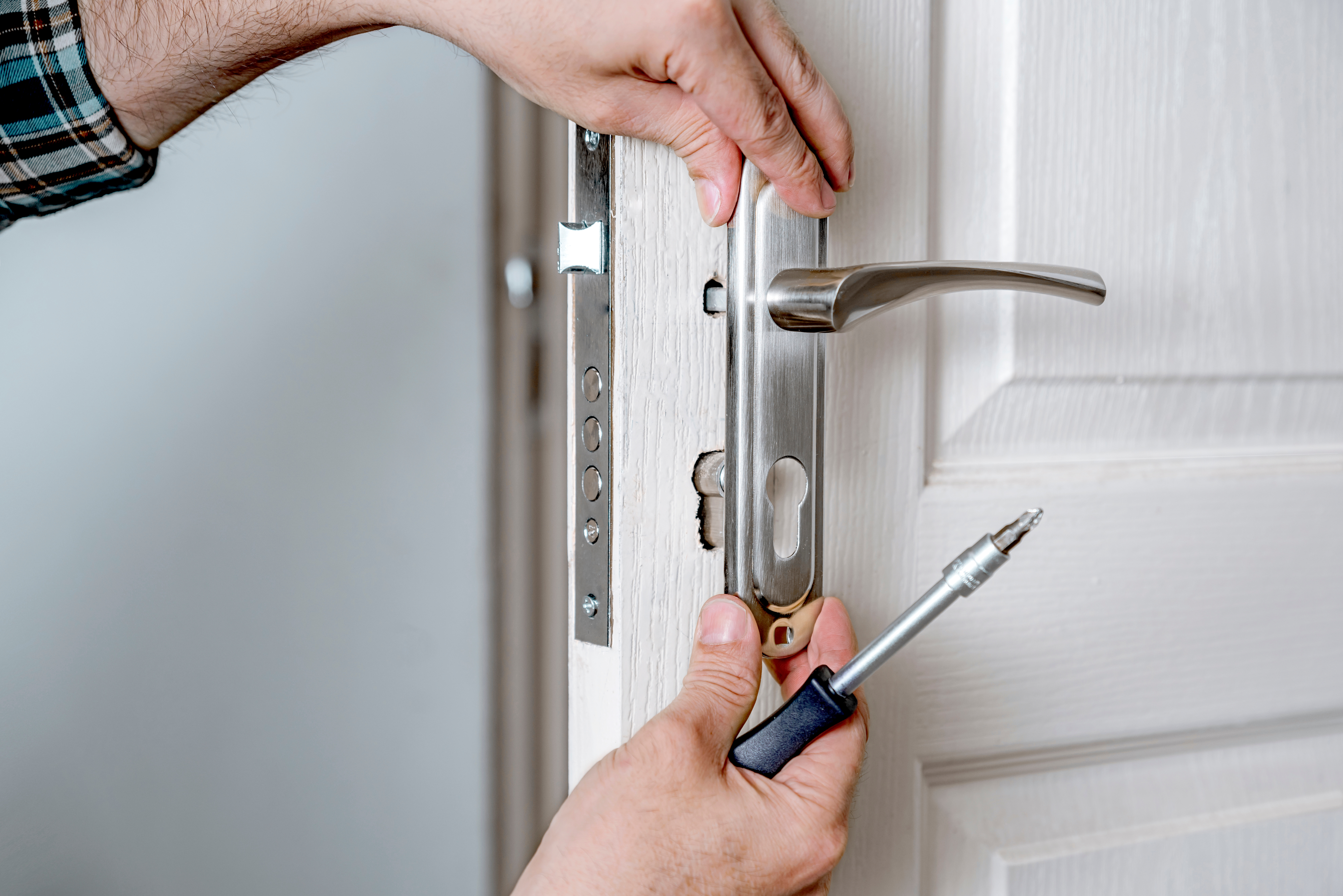 Person installing a door handle and lockset on a white interior door during the final phase of door installation.