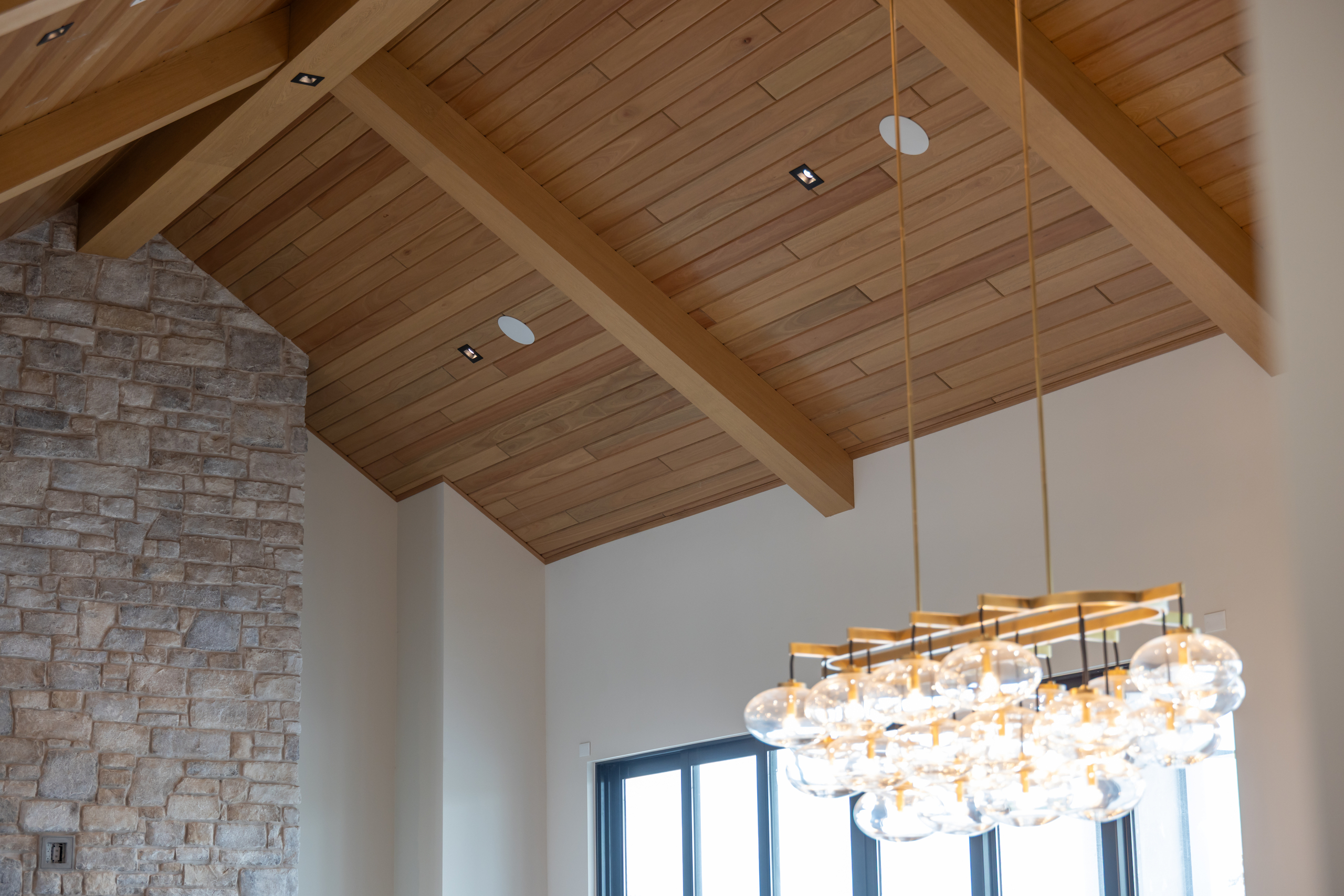 Vaulted ceiling with warm wood panels and exposed beams above a stone fireplace wall.