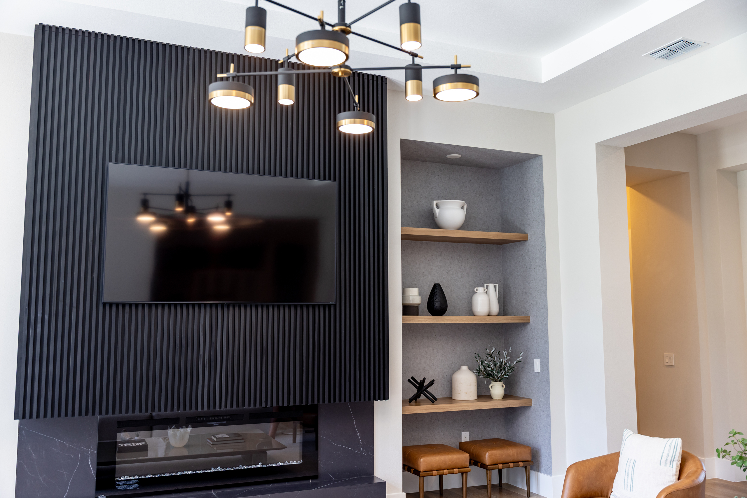 Contemporary living space with a black slatted accent wall, modern chandelier, and custom millwork shelving by 1st Choice Door & Millwork.