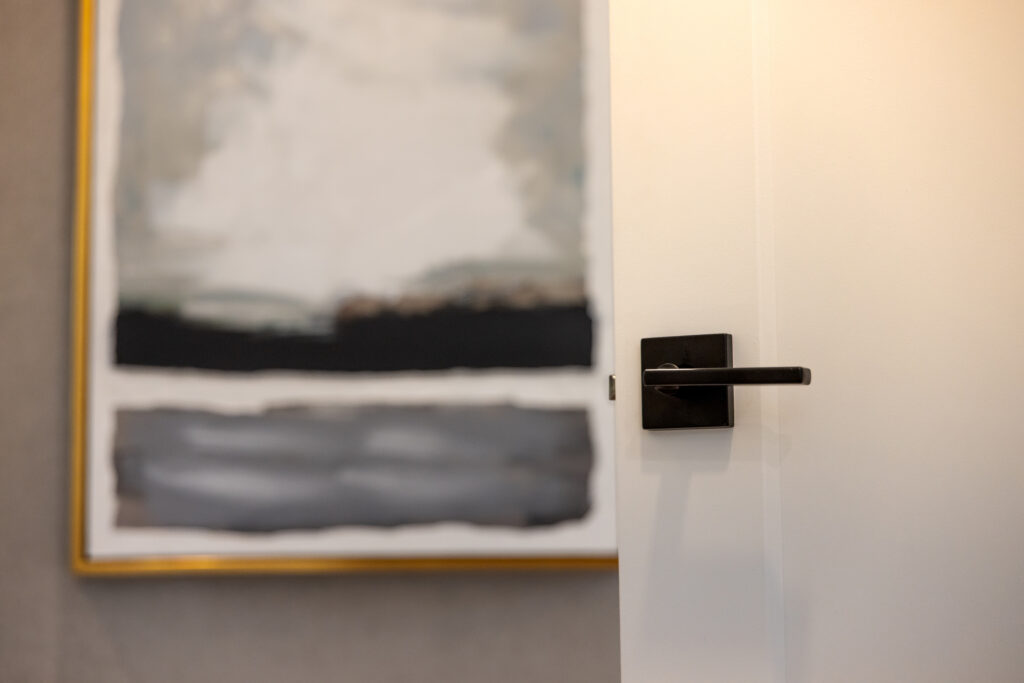 Close-up of a matte black door handle on a white interior door, with a blurred abstract painting in the background.