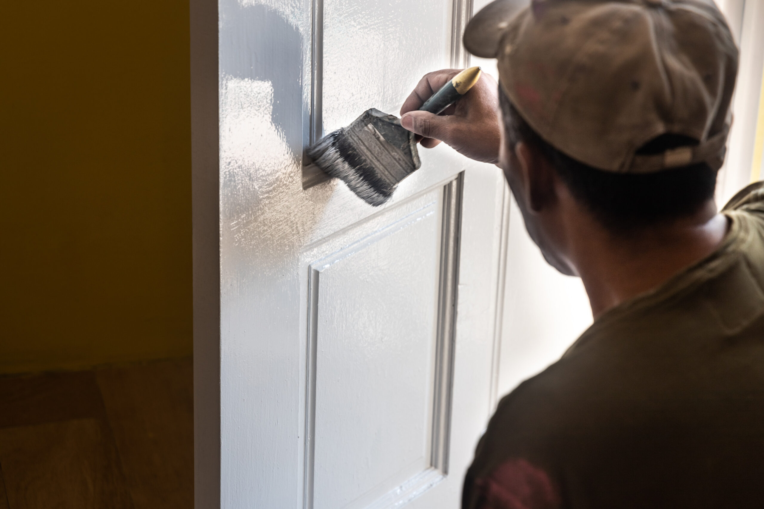 Painted vs. Stained: Which is Best for Custom Interior Doors? 1 Person painting a white interior door with a brush, applying an even coat for a smooth painted finish.