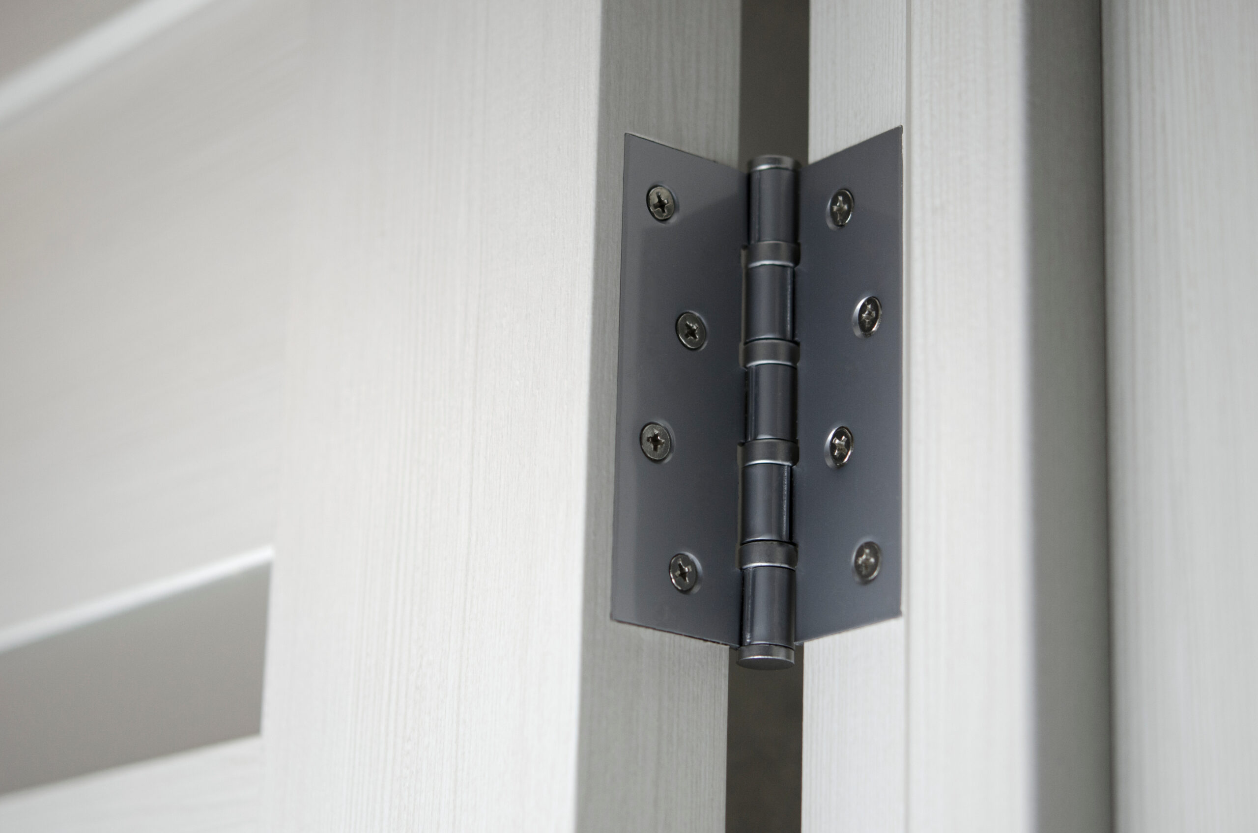 Close-up of a black interior door hinge on a light-colored door and frame.